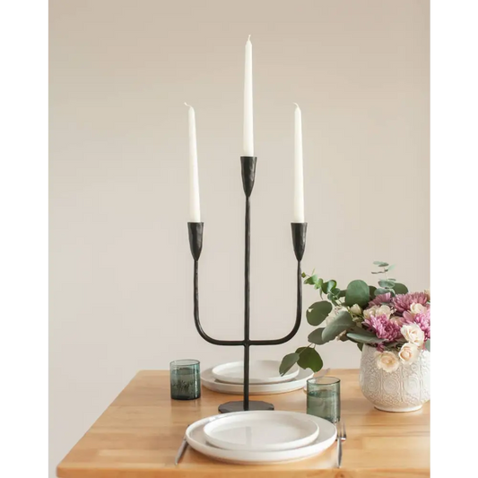 Black hand-forged iron three-arm candelabra with white taper candles