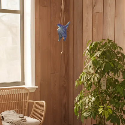 A handcrafted blue bird flying mobile features a blue bird wind chime with a metallic finish hanging on a wooden wall