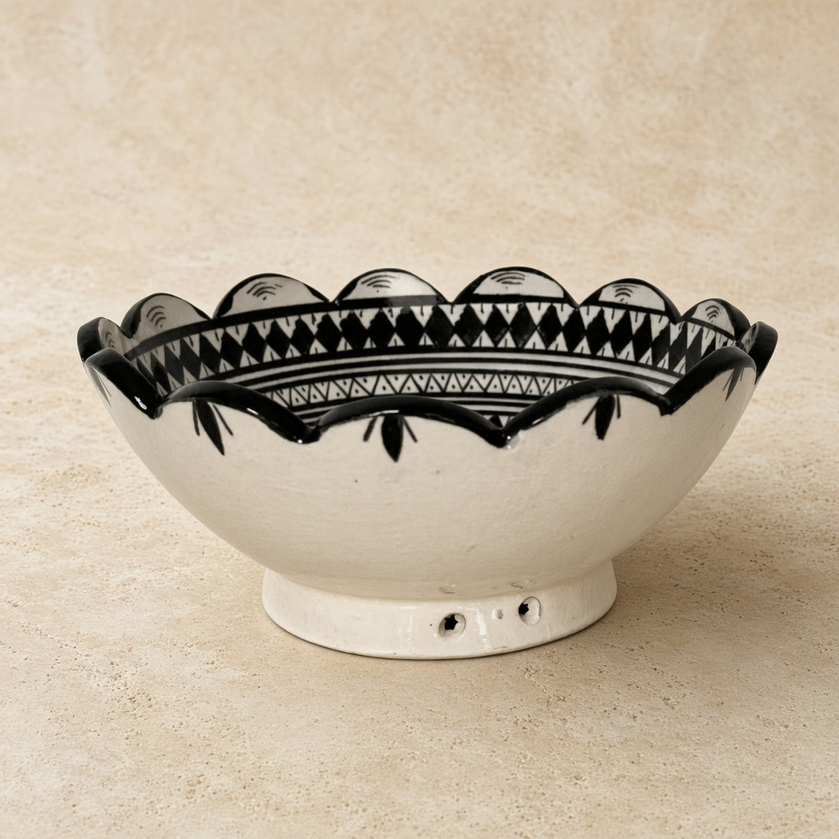 A handcrafted ceramic bowl from safi morocco with black geometric patterns and small base indentations inspired by rugged atlantic