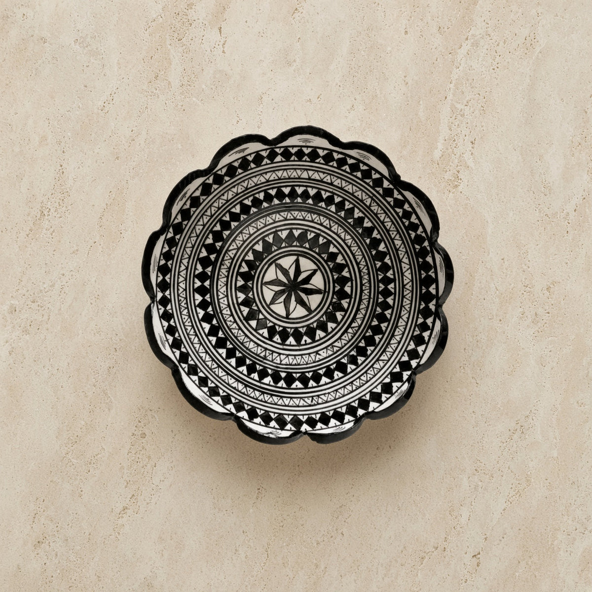 Handcrafted ceramic bowl from safi morocco with black geometric patterns and a scalloped edge inspired by rugged atlantic