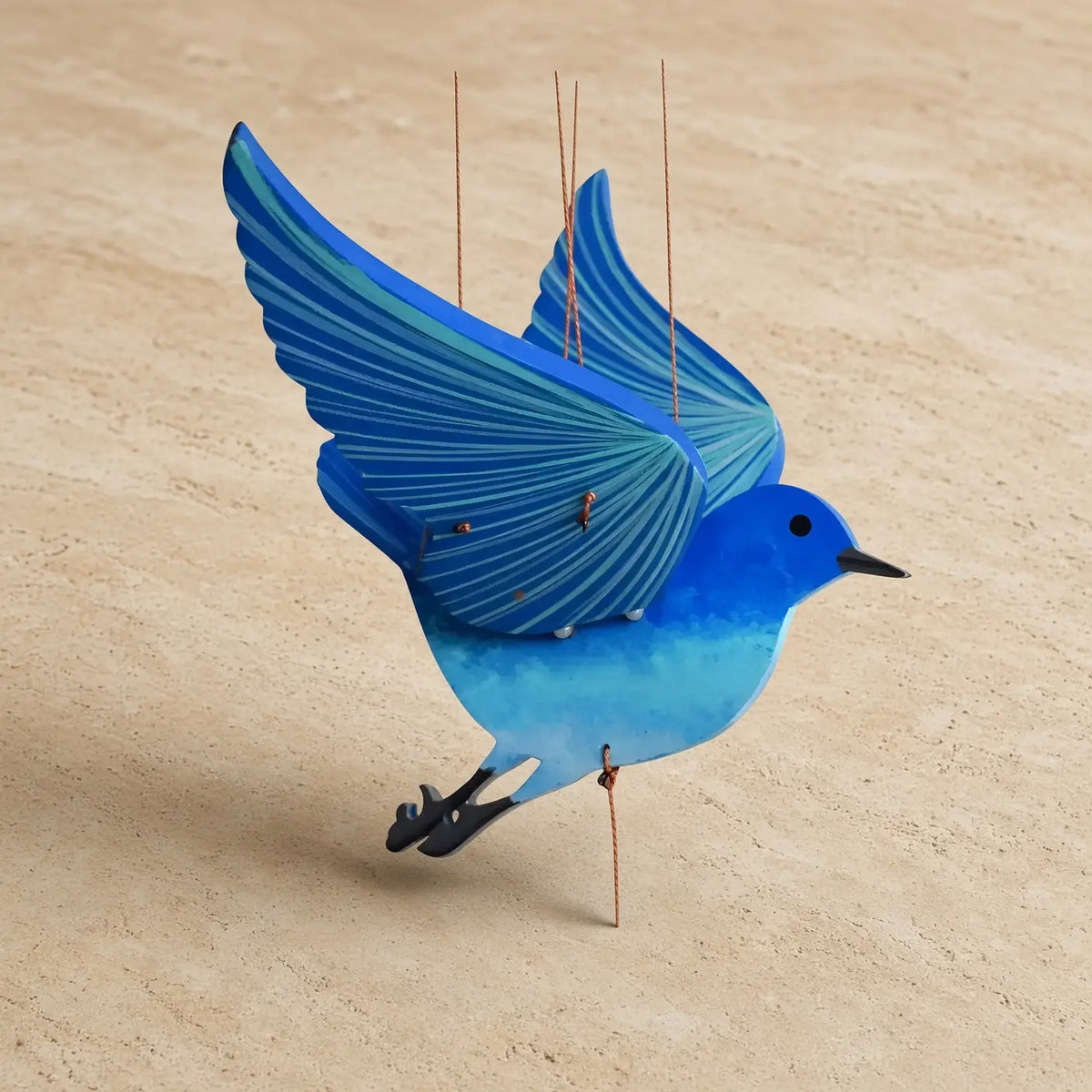 A handcrafted flying bluebird kinetic mobile featuring a vibrant blue wooden bird with detailed wing stripes and black feet suspended by thin strings perfectly balanced