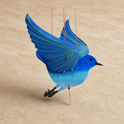 A handcrafted flying bluebird kinetic mobile featuring a vibrant blue wooden bird with detailed wing stripes and black feet suspended by thin strings perfectly balanced