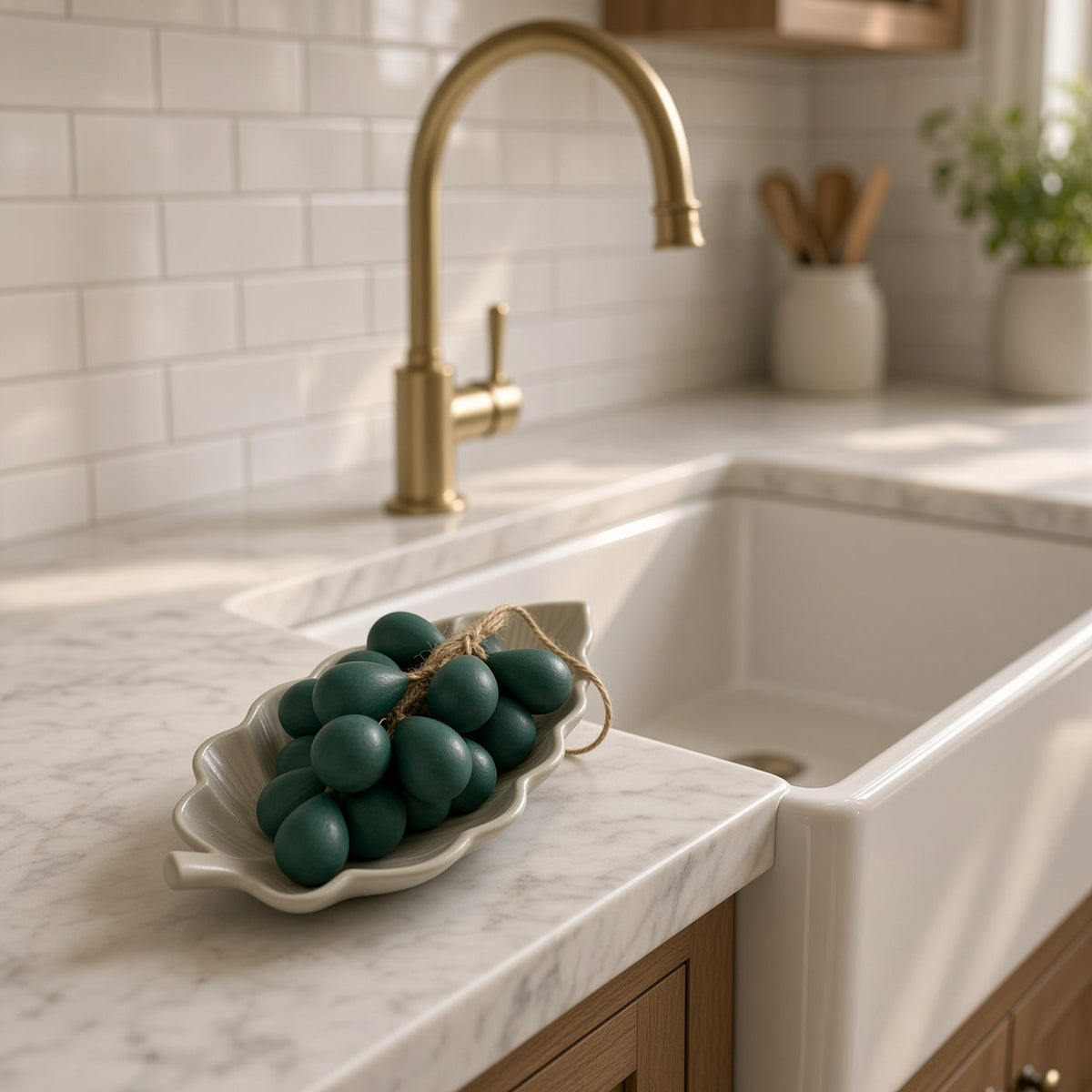 A white ceramic leaf bowl holding dark green twine tied decorative eggs next to handcrafted grape cluster olive oil soap