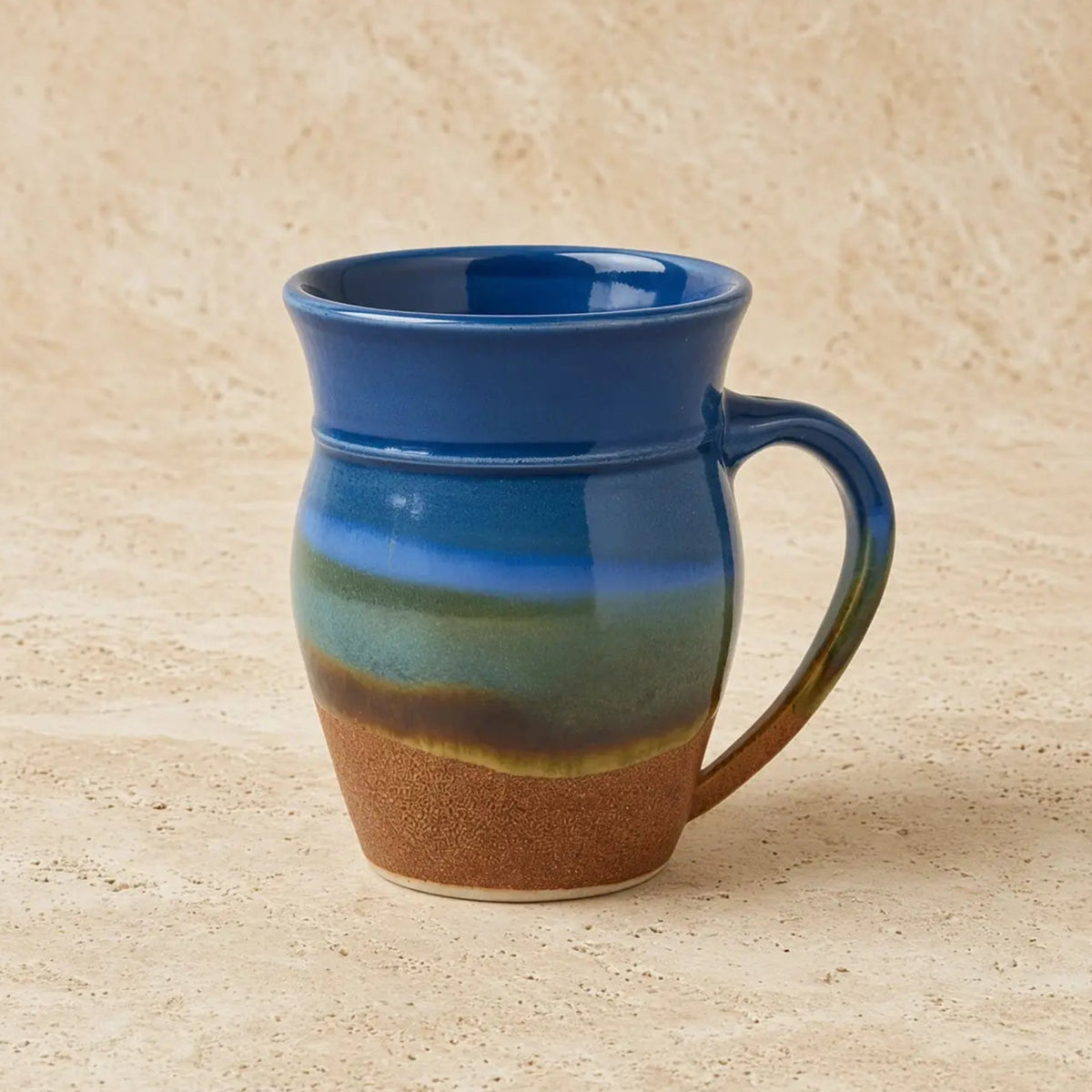 A handcrafted pottery mug with a gradient glaze dances from deep blue to earthy brown capturing sky vibes