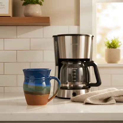 Handcrafted pottery mug with gradient glaze dances from deep blue to green and brown featuring the mugs unique sturdy handle