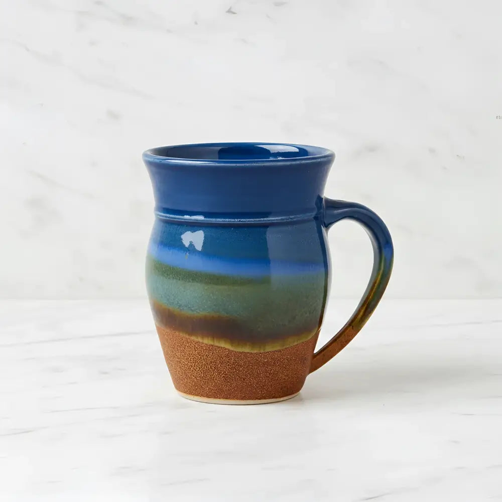 Handcrafted pottery mug with gradient glaze dances from deep blue to green and brown featuring a sturdy handle