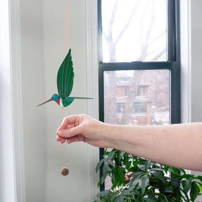 A handmade eco-friendly hummingbird flying mobile in green with a turquoise head and red throat from a woman-owned business