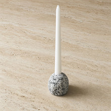 A sleek white taper candle in a handcrafted stone taper candle holder made of speckled gray stone