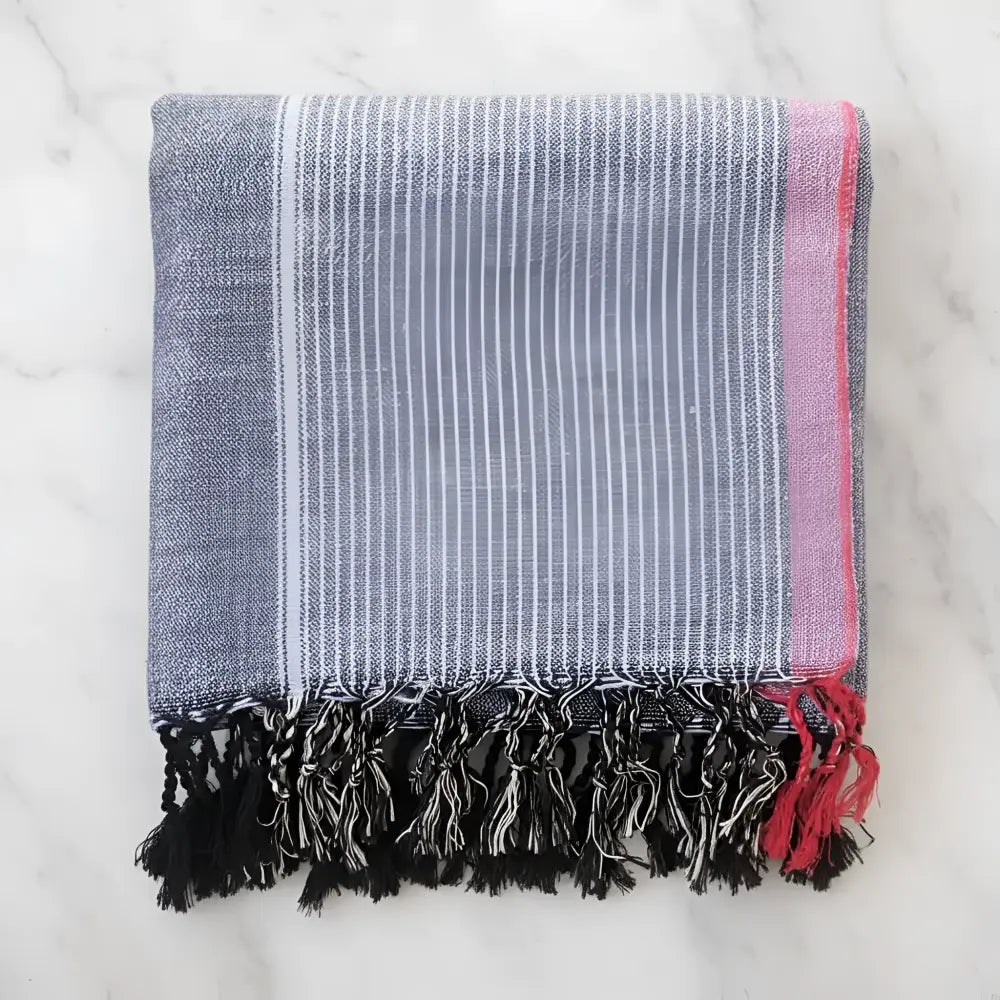 Folded handmade turkish cotton hand towel with indigo tribeca blue white stripes pink border and black tassels