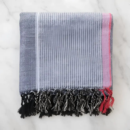 Folded handmade turkish cotton hand towel with indigo tribeca blue white stripes pink border and black tassels