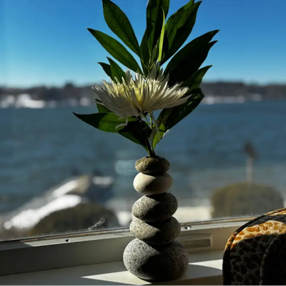 Handmade eco-friendly cairn vase with stacked gray stones, white flower, and green leaves