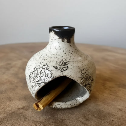 Handmade ceramic birdhouse incense burner with black floral design holding palo santo stick
