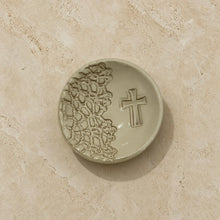 A beige ceramic handmade cross ring dish with a raised cross and lace pattern perfect as a unique gift for jewelry