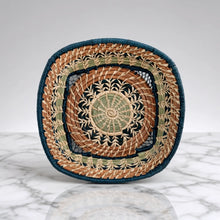 Handmade guatemalan basket with a colorful woven pattern in tan green and dark blue strands and a blue rim