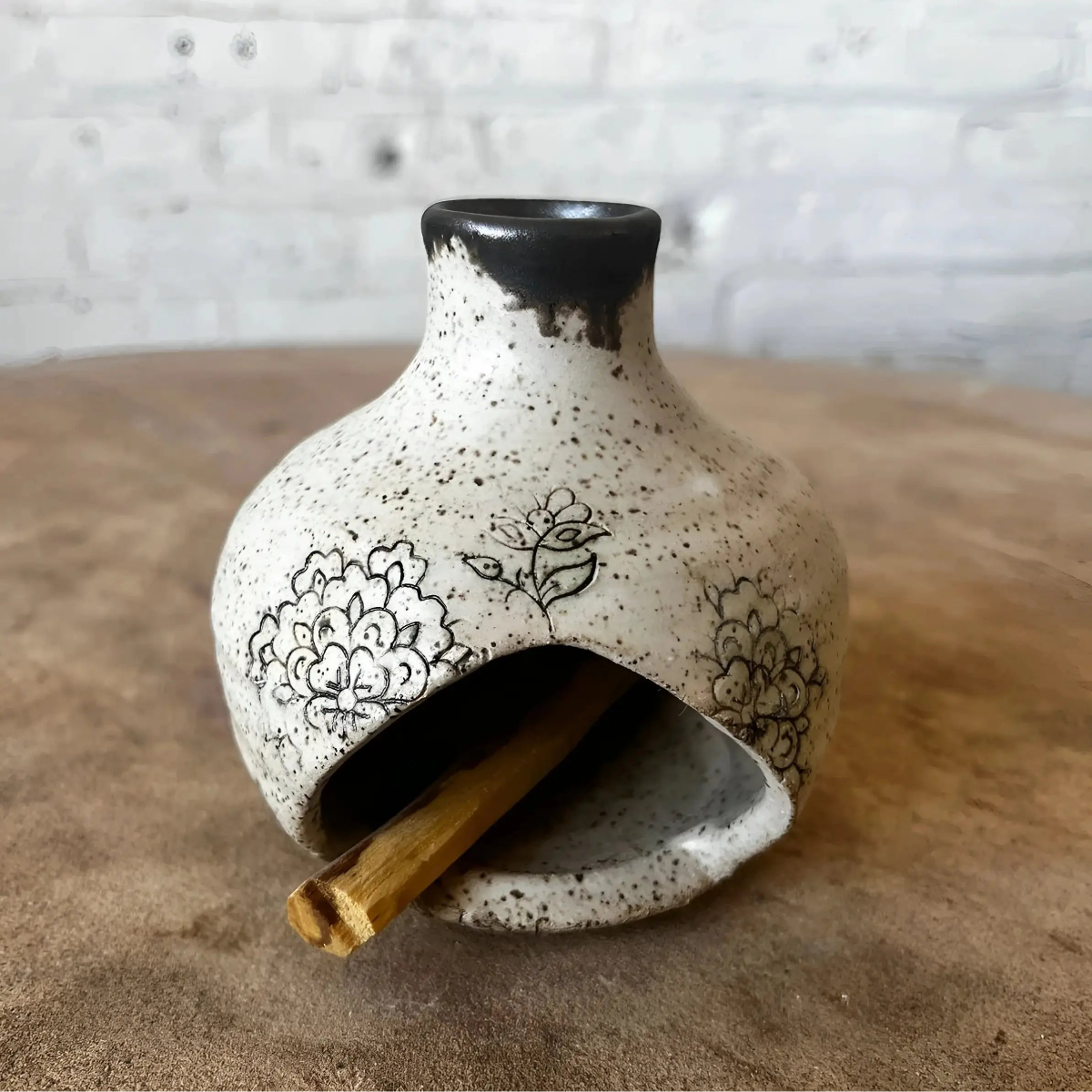 Handmade ceramic birdhouse incense burner with black floral design holding palo santo stick