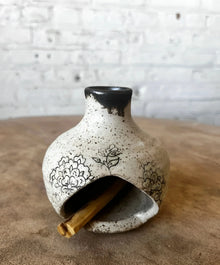 Handmade ceramic birdhouse incense burner with black floral design holding palo santo stick
