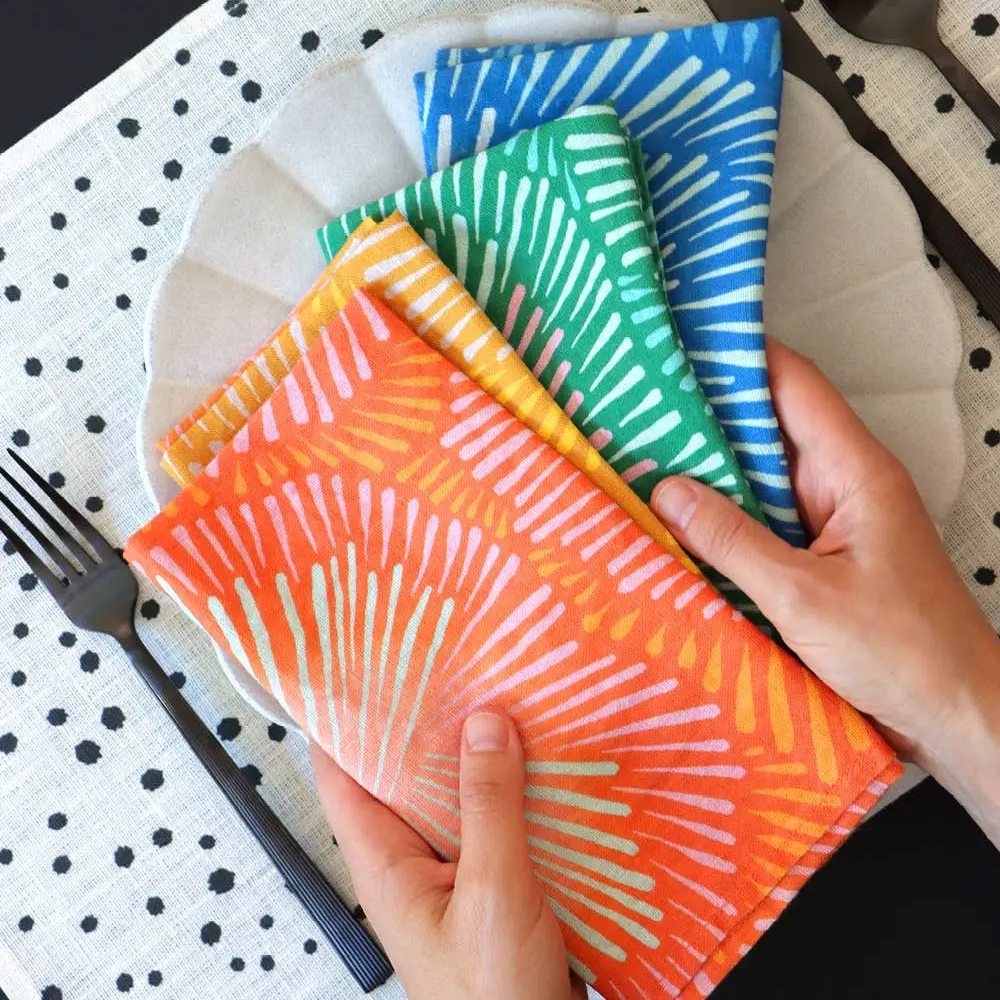A stack of handmade european linen napkins in bright colors set with sunburst patterns in orange yellow green and blue