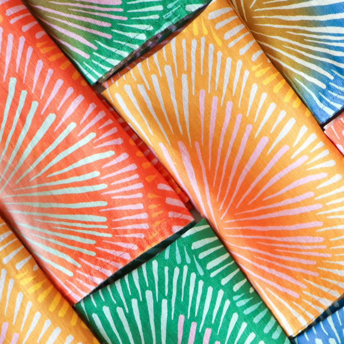 Handmade european linen napkins in bright colors set with vibrant orange and green sunburst pattern for lively table decor
