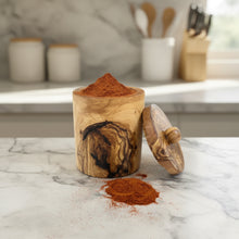 Handmade eco-friendly olivewood spice jar overflowing with reddish-brown powder spilled nearby