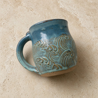 Handmade pottery mug with textured teal blue glaze and raised metallic wave design perfect for coffee lovers