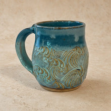 Handmade pottery mug with vibrant teal blue glaze and earthy gold wave design for unique coffee moments