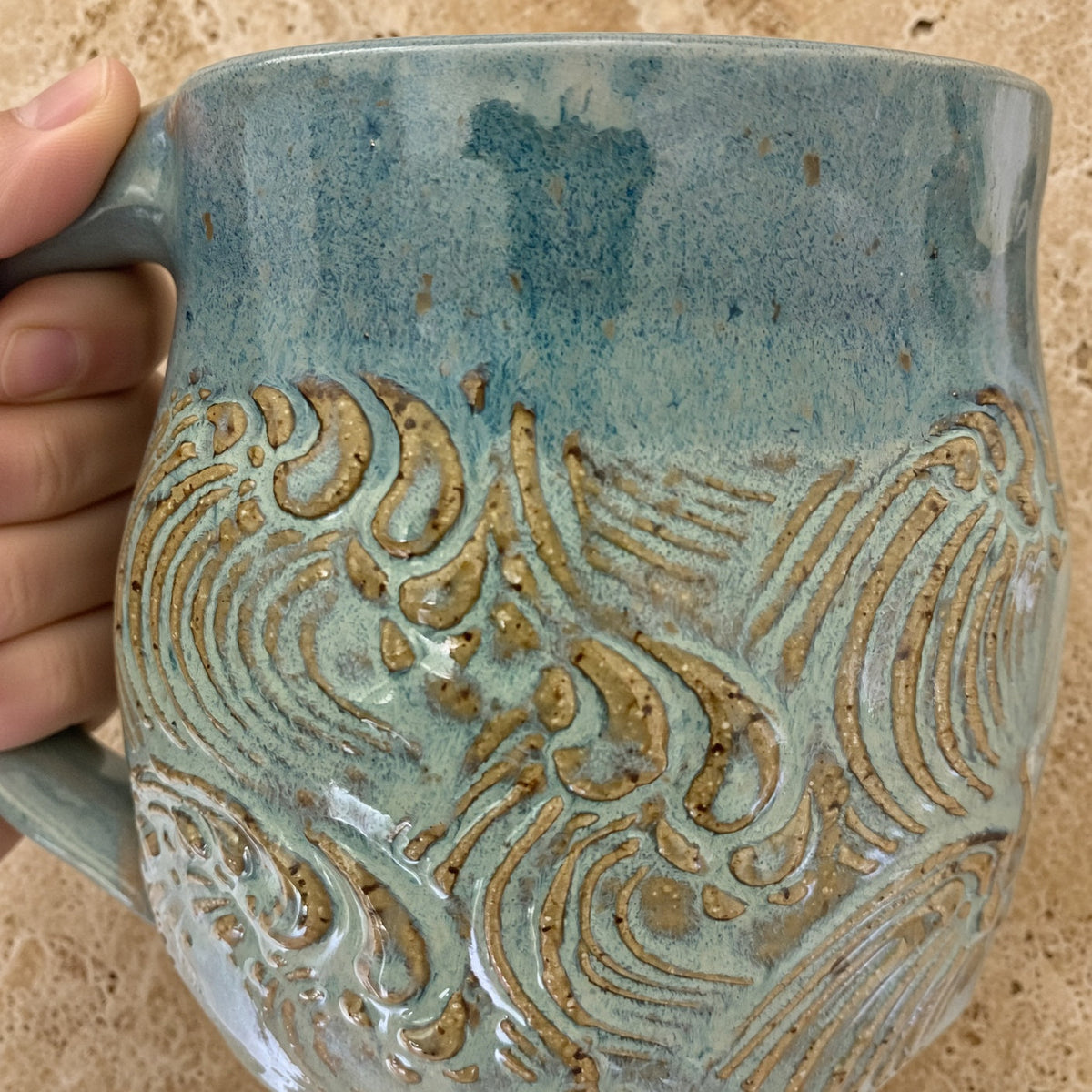 Handmade pottery mug with a textured teal blue mug glaze and raised golden-brown wave design patterns