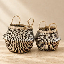 Two handmade seagrass belly baskets with black zig-zag patterns and sturdy handles in natural beige and black