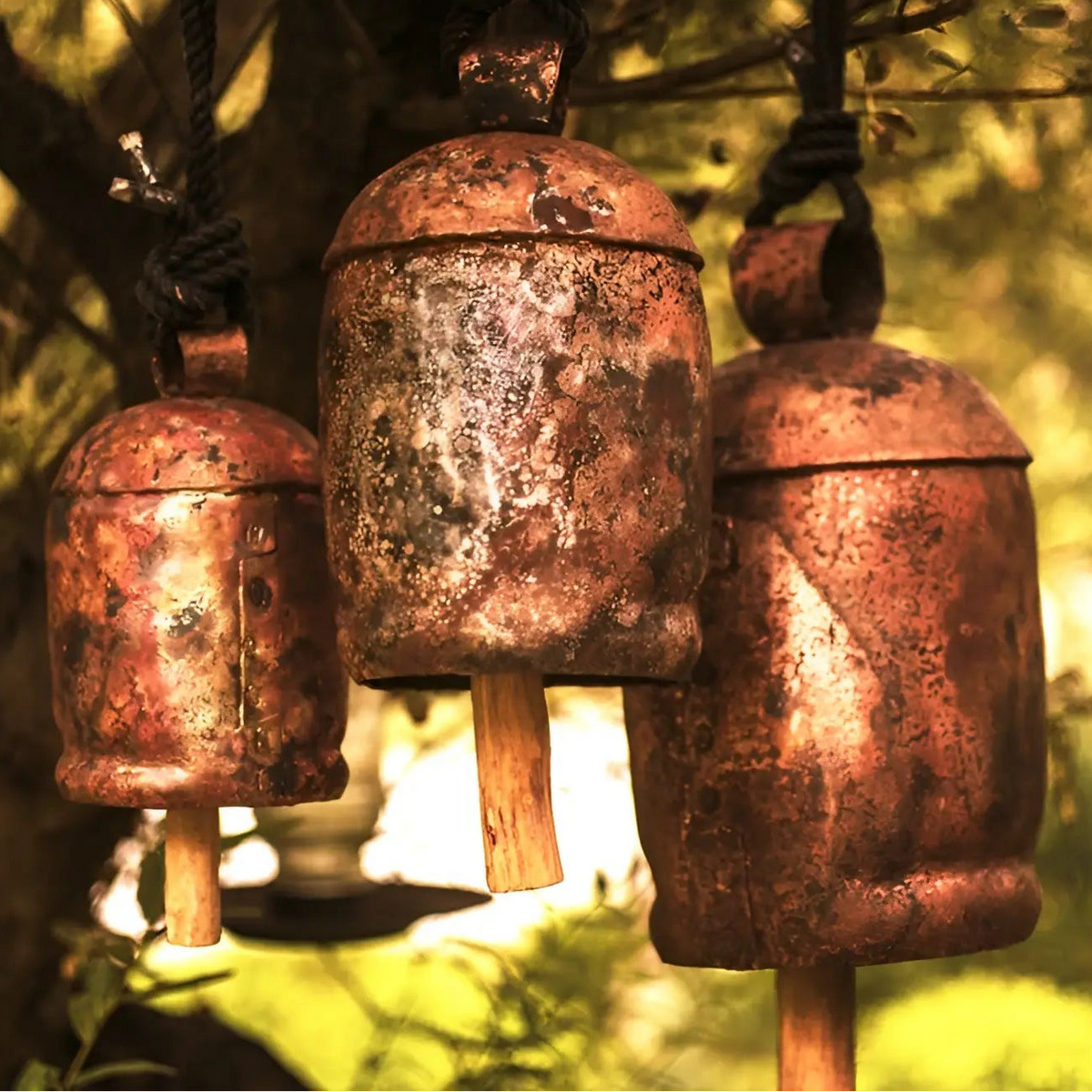 Three handmade solo copper large copper zen bells with wooden bead accents hang outdoors with rustic weathered look