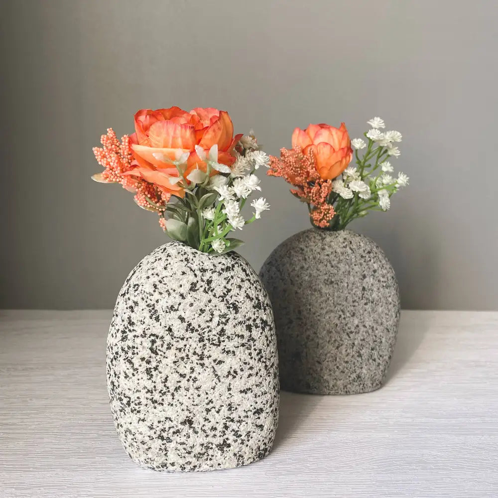 Handmade stone vase with orange flowers and white filler on gray background