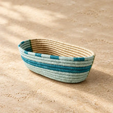 An oval handwoven sisal bread basket with teal and light blue stripes and a natural beige interior for serving essentials