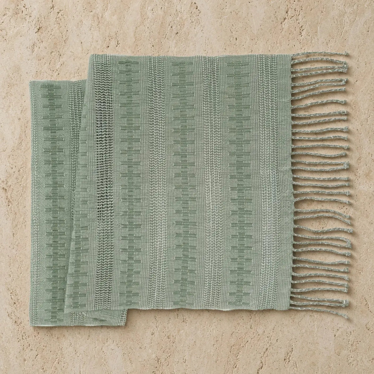 A soft sage green handwoven calado table runner with textured pattern and fringed edges for dining decor