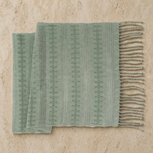 A soft sage green handwoven calado table runner with textured pattern and fringed edges for dining decor