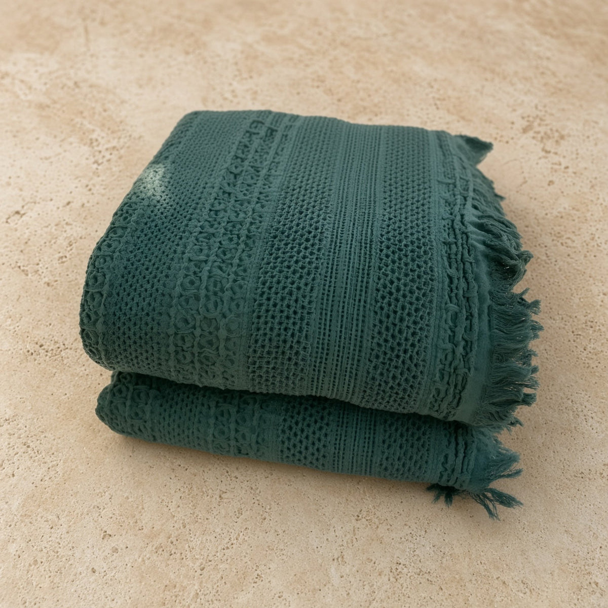 A folded dark green handwoven waffle bed blanket with fringed edges and textured cotton woven pattern