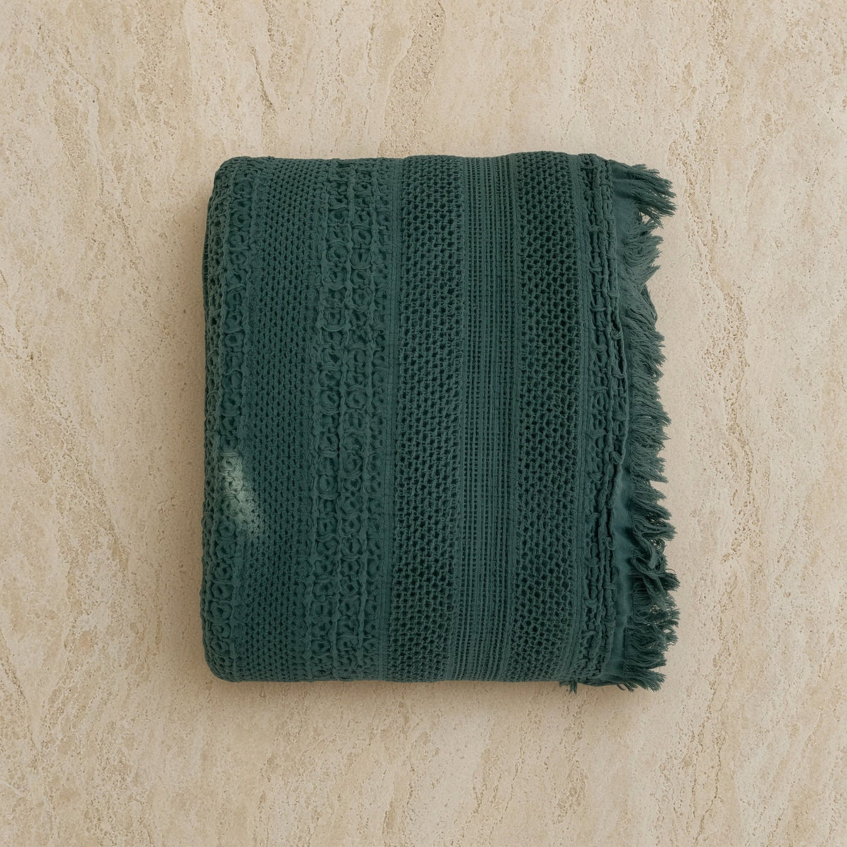 A folded dark green handwoven waffle bed blanket with frayed edges and intricate woven cotton patterns