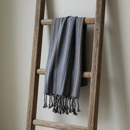 A handwoven earthy striped kekova towel with fringe hangs draped on a rustic ladder effortlessly combining style
