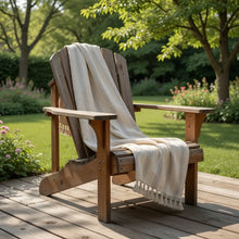 A rustic wooden adirondack chair with a handwoven linen-cotton blend turkish towel featuring light brown stripes draped over it
