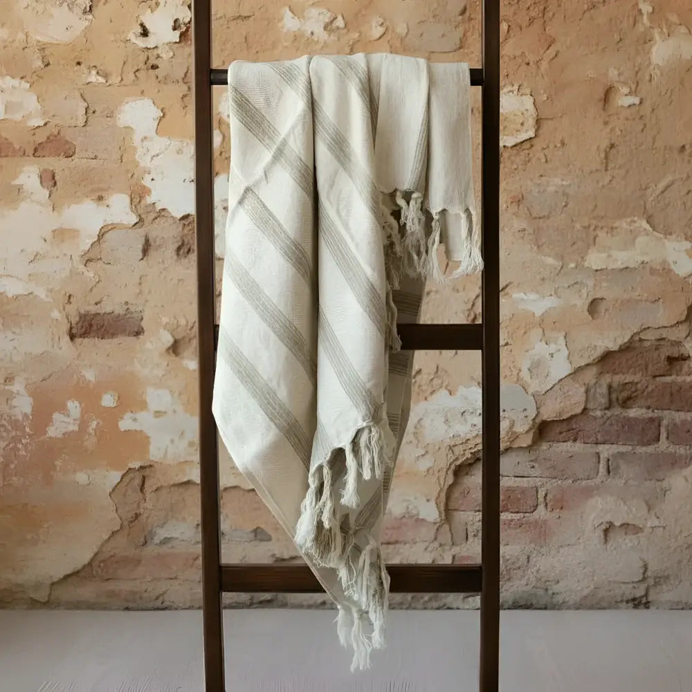 Cream gray striped tassel blanket on ladder by brick wall