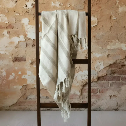 Cream gray striped tassel blanket on ladder by brick wall