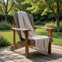 A rustic wooden adirondack chair with a handwoven linen-cotton blend turkish towel featuring light brown stripes draped over it