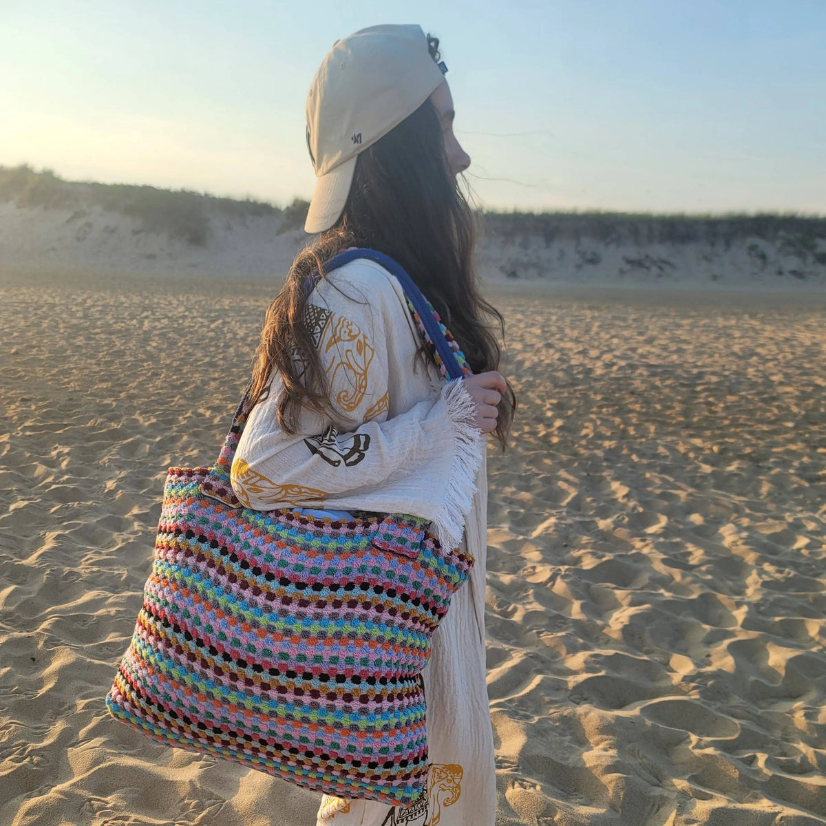 Woman with a patterned long sleeve top and beige cap carrying a large multicolor tote bag
