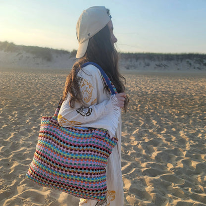 Woman with a patterned long sleeve top and beige cap carrying a large multicolor tote bag