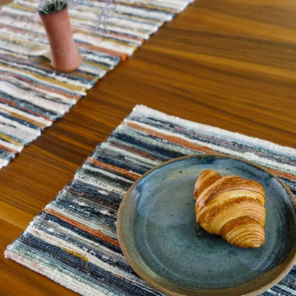 Flaky golden-brown croissant on a handwoven upcycled fabric placemat on a blue ceramic plate