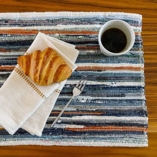 Adesé Handwoven Upcycled Fabric Placemat on wood surface with croissant and cup of coffee