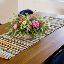 A vibrant floral arrangement in a rustic stone vase on a handwoven upcycled fabric table runner with earthy stripes