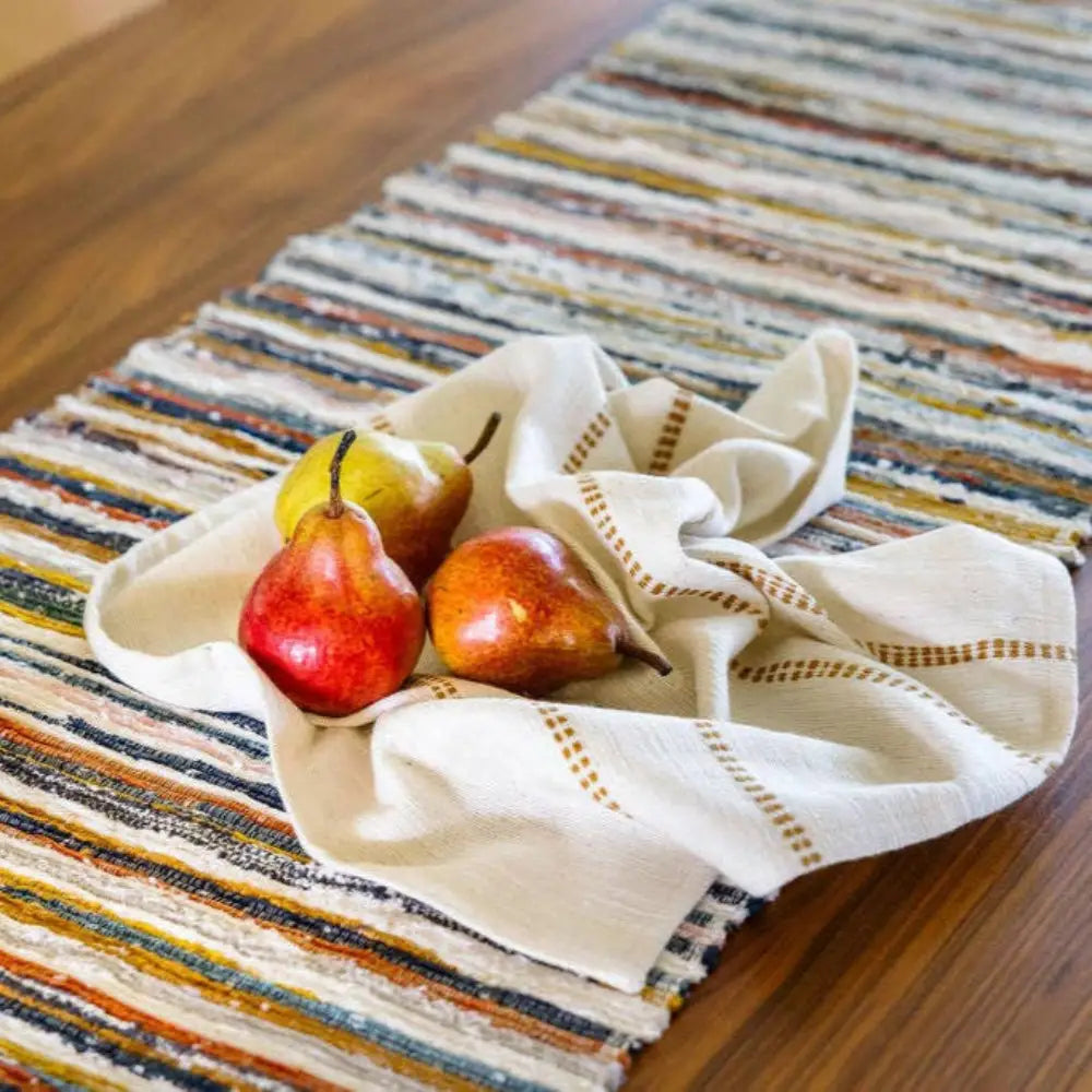 Handwoven Upcycled Fabric Table runner on a wooden table with three pears and a cloth napkin