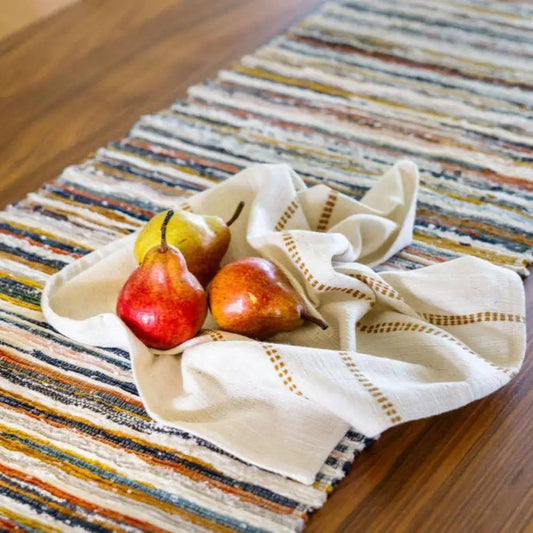 Handwoven Upcycled Fabric Table runner on a wooden table with three pears and a cloth napkin