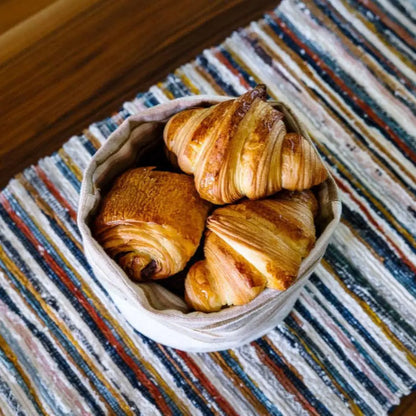 Handwoven Upcycled Fabric Table Runner striped on a wooden surface with a basket of croissants