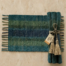 A handwoven vetiver placemat in teal and green gradient with fringed edges tied with natural fiber rope and tassels