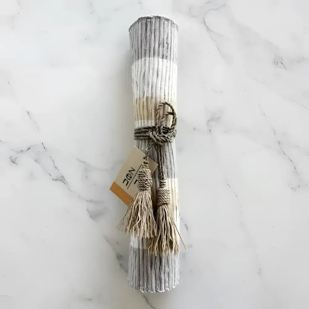 A rolled-up handwoven vetiver table runner in gray and beige stripes tied with rustic twine and tassels