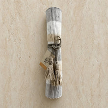 A rolled handwoven vetiver table runner in soft gray and beige stripes tied with rustic twine and tassels